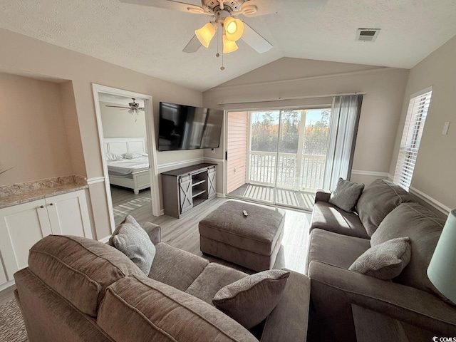 living room with ceiling fan, vaulted ceiling, a textured ceiling, and light wood-type flooring