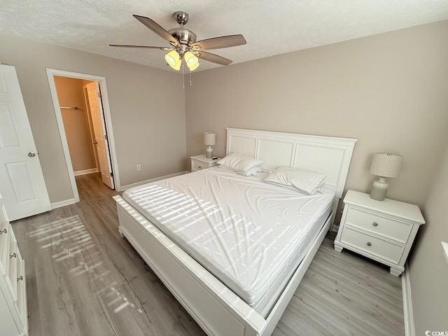 bedroom with light hardwood / wood-style flooring, ceiling fan, a textured ceiling, a spacious closet, and a closet