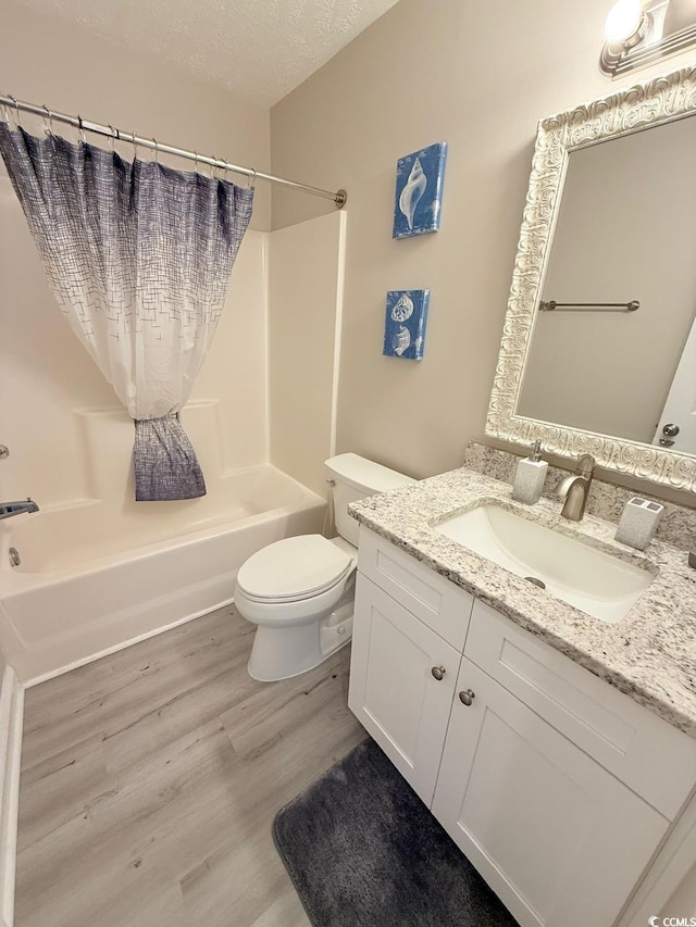 full bathroom with hardwood / wood-style floors, vanity, toilet, a textured ceiling, and washtub / shower combination