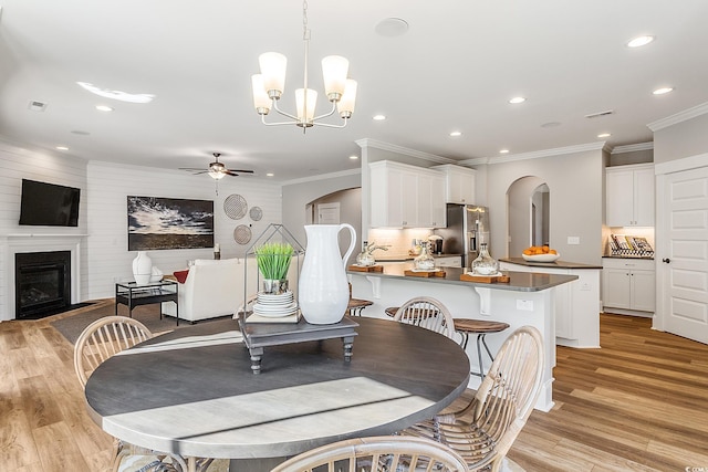 dining area with ceiling fan with notable chandelier, sink, crown molding, light hardwood / wood-style flooring, and a large fireplace