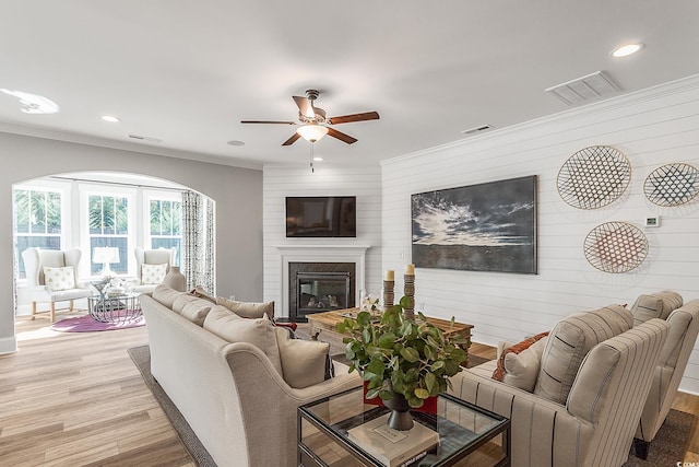 living room with light hardwood / wood-style flooring, ceiling fan, ornamental molding, and wood walls