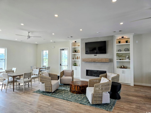 living room featuring wood-type flooring, a large fireplace, plenty of natural light, and ceiling fan