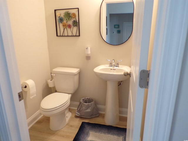 half bathroom with a sink, baseboards, toilet, and wood finished floors