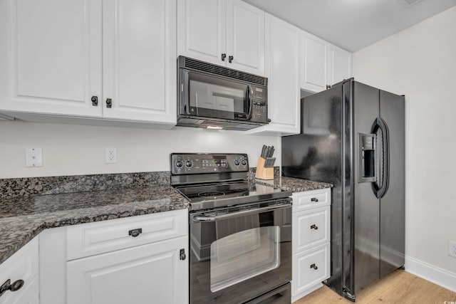 kitchen with black appliances, white cabinets, light wood-type flooring, and dark stone countertops