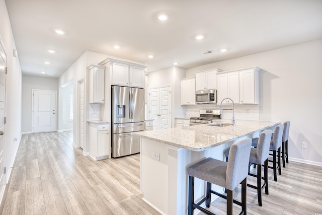 kitchen featuring kitchen peninsula, appliances with stainless steel finishes, a kitchen breakfast bar, light hardwood / wood-style floors, and white cabinetry