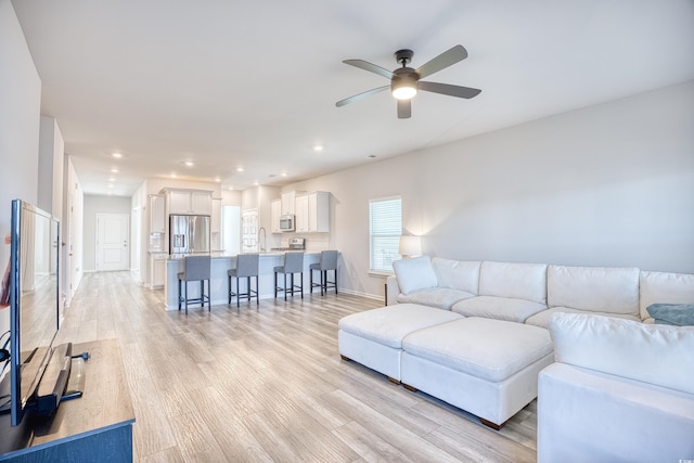 living room featuring ceiling fan, sink, and light wood-type flooring