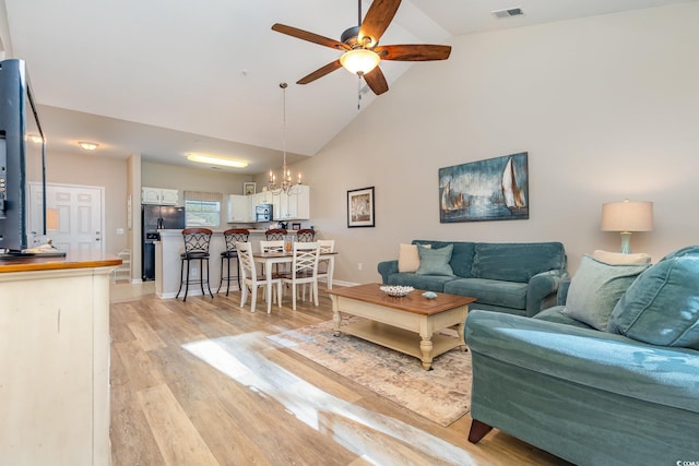 living room featuring ceiling fan with notable chandelier, light hardwood / wood-style floors, and high vaulted ceiling