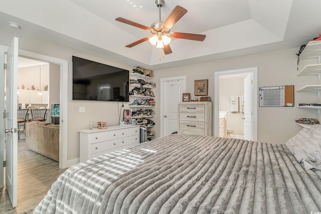 bedroom featuring light wood-type flooring, a tray ceiling, ceiling fan, and ensuite bathroom