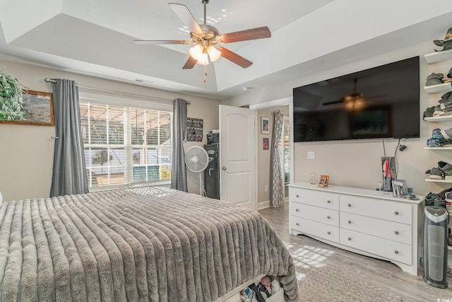 bedroom featuring light hardwood / wood-style flooring, a raised ceiling, and ceiling fan