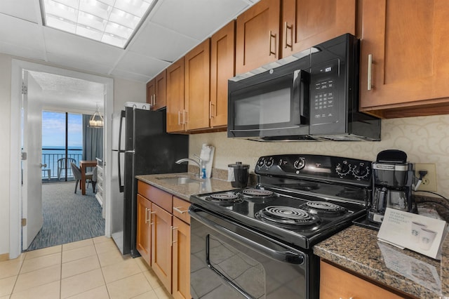 kitchen with sink, a water view, light tile patterned flooring, dark stone counters, and black appliances