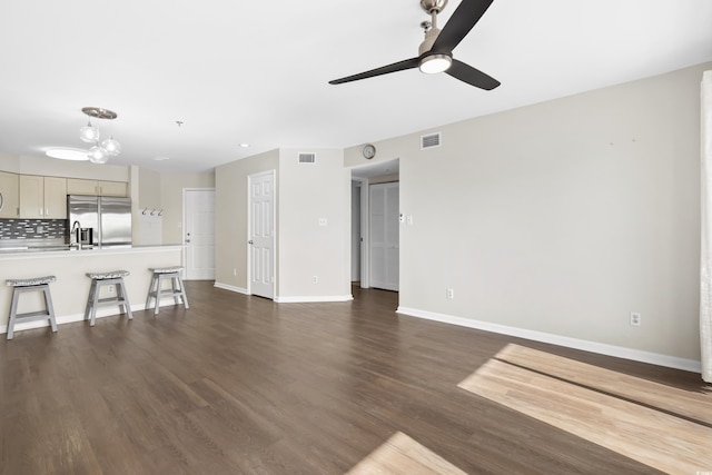 unfurnished living room featuring ceiling fan with notable chandelier and dark wood-type flooring