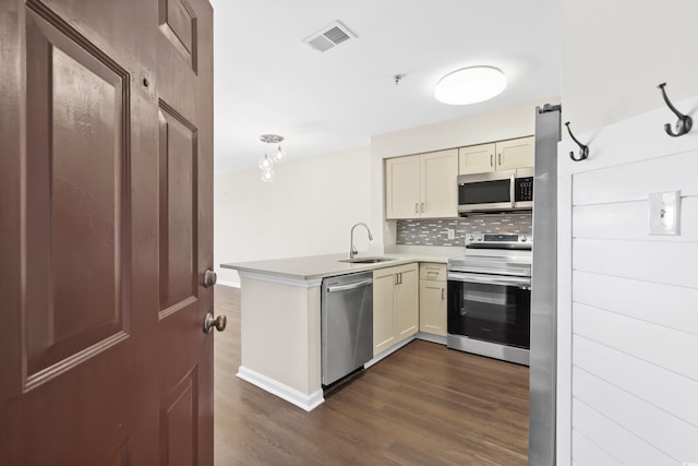 kitchen with kitchen peninsula, dark hardwood / wood-style flooring, stainless steel appliances, sink, and cream cabinetry