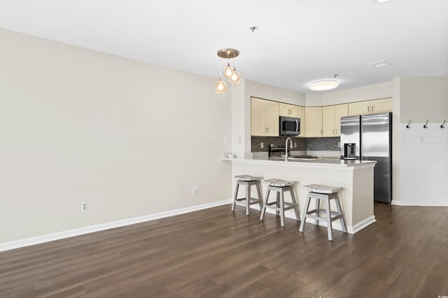 kitchen featuring dark wood-type flooring, cream cabinets, decorative backsplash, kitchen peninsula, and stainless steel appliances