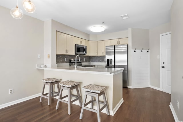 kitchen with hanging light fixtures, dark wood-type flooring, tasteful backsplash, cream cabinetry, and appliances with stainless steel finishes