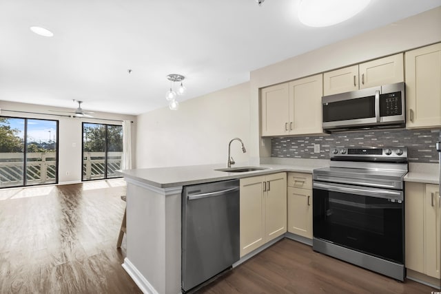 kitchen with sink, backsplash, kitchen peninsula, cream cabinets, and appliances with stainless steel finishes