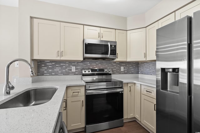 kitchen with decorative backsplash, light stone counters, stainless steel appliances, sink, and cream cabinetry