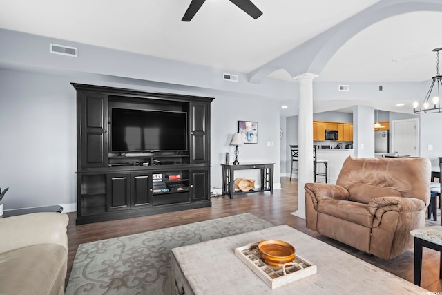 living room with ceiling fan with notable chandelier, lofted ceiling, dark wood-type flooring, and decorative columns