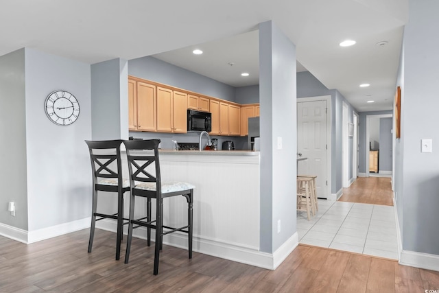 kitchen with kitchen peninsula, light brown cabinetry, light wood-type flooring, a breakfast bar, and sink