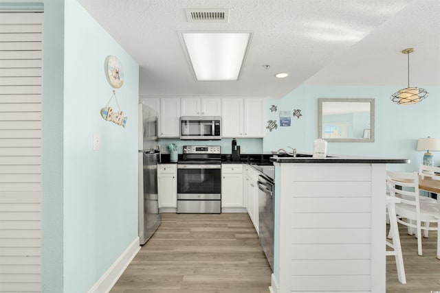 kitchen featuring kitchen peninsula, white cabinets, hanging light fixtures, and appliances with stainless steel finishes