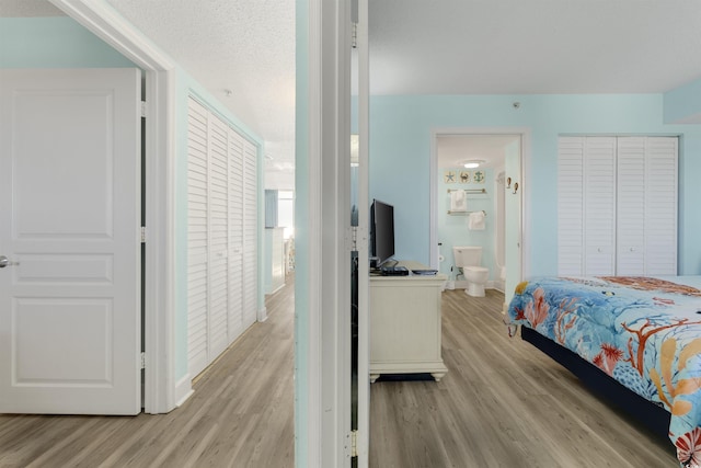 bedroom with a textured ceiling, connected bathroom, and light hardwood / wood-style flooring