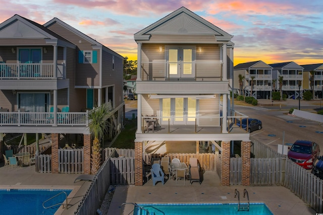 back house at dusk featuring french doors, a patio area, a balcony, and a fenced in pool