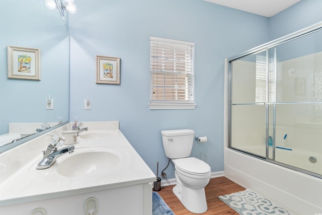 full bathroom featuring hardwood / wood-style flooring, bath / shower combo with glass door, toilet, and vanity