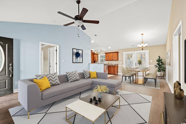 living room featuring french doors, ceiling fan with notable chandelier, lofted ceiling, and light wood-type flooring