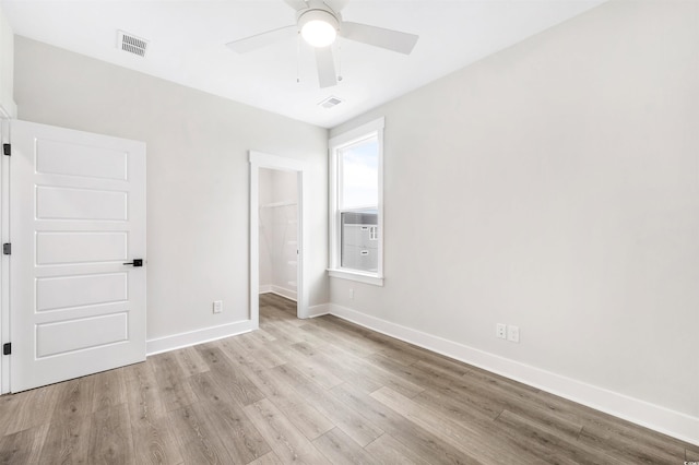 unfurnished bedroom featuring cooling unit, light hardwood / wood-style flooring, a spacious closet, ceiling fan, and a closet