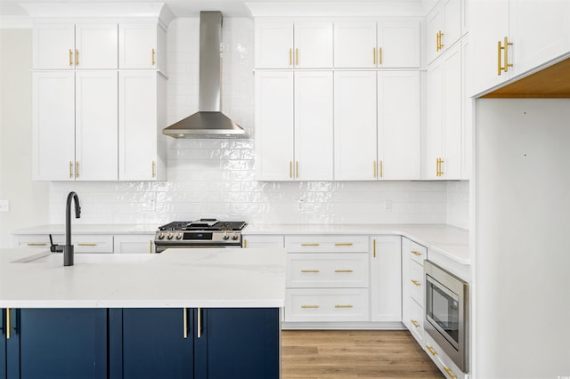 kitchen with wall chimney range hood, white cabinets, and appliances with stainless steel finishes