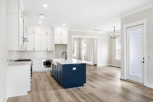 kitchen with stainless steel microwave, decorative light fixtures, white cabinets, blue cabinetry, and a center island with sink