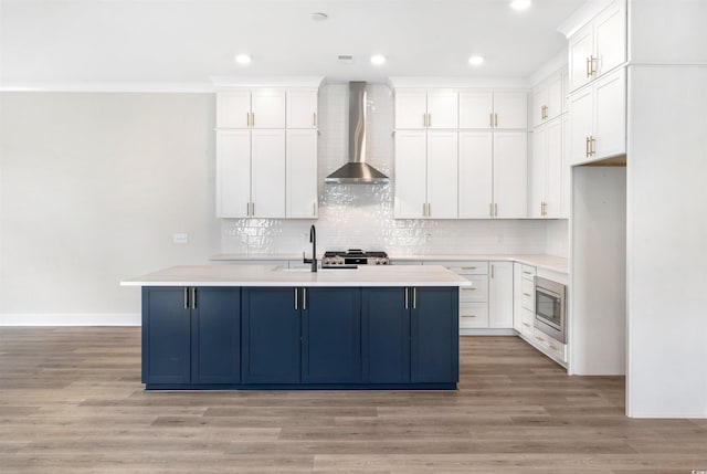 kitchen featuring white cabinetry, stainless steel microwave, wall chimney exhaust hood, and light wood-type flooring