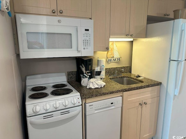 kitchen featuring light brown cabinets, dark stone countertops, white appliances, and sink