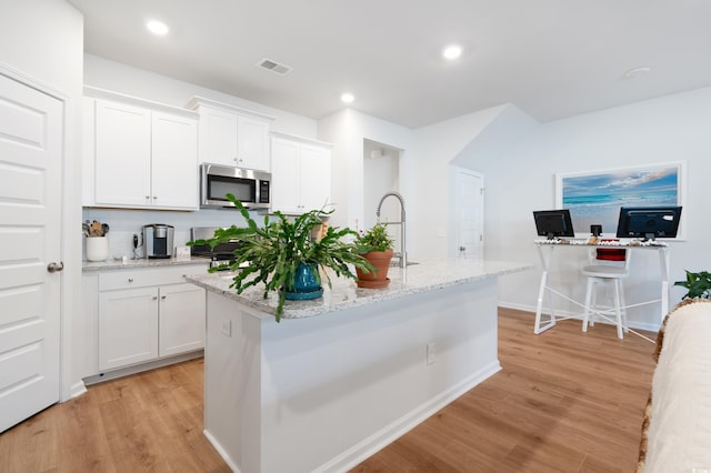 kitchen featuring light wood-type flooring, light stone counters, a kitchen island with sink, sink, and white cabinetry