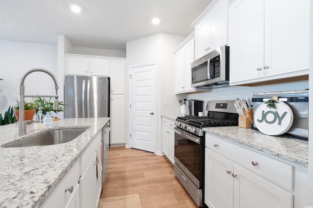 kitchen with light stone countertops, white cabinetry, sink, and stainless steel appliances