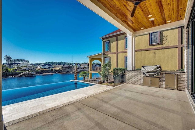 view of swimming pool with ceiling fan, a patio area, a water view, and exterior kitchen