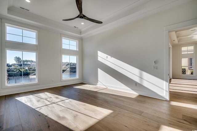 unfurnished living room with hardwood / wood-style flooring, ceiling fan, a raised ceiling, ornamental molding, and a water view