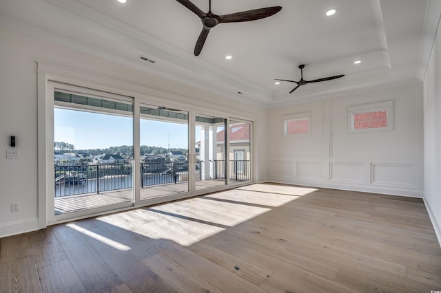 spare room with ceiling fan, a tray ceiling, light hardwood / wood-style flooring, and a water view