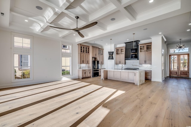 kitchen featuring decorative light fixtures, backsplash, wall chimney range hood, coffered ceiling, and a large island