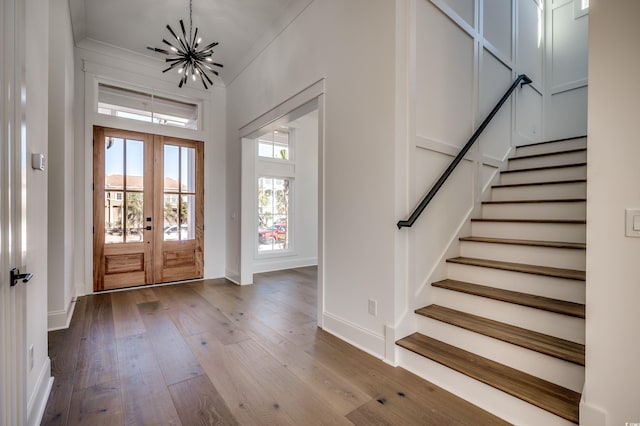 entryway with hardwood / wood-style floors, crown molding, french doors, and an inviting chandelier