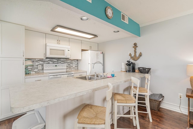 kitchen featuring white appliances, dark wood-type flooring, a kitchen breakfast bar, kitchen peninsula, and white cabinetry