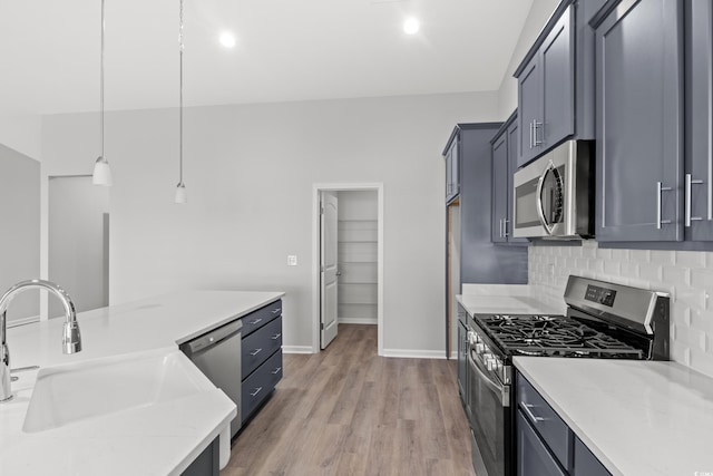 kitchen with sink, hanging light fixtures, light stone countertops, light wood-type flooring, and appliances with stainless steel finishes