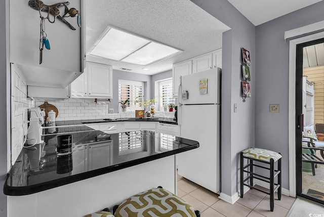 kitchen featuring kitchen peninsula, white cabinetry, light tile patterned flooring, and white refrigerator