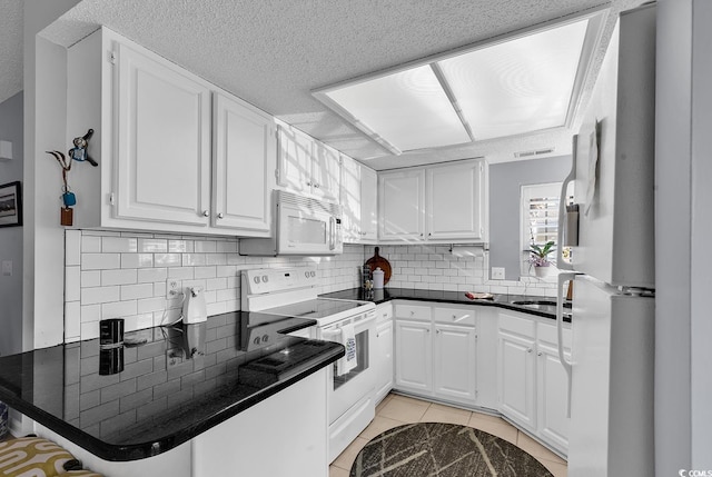 kitchen with kitchen peninsula, white appliances, white cabinets, and light tile patterned flooring