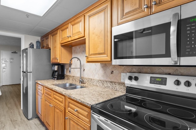 kitchen featuring sink, decorative backsplash, light stone countertops, appliances with stainless steel finishes, and light hardwood / wood-style floors