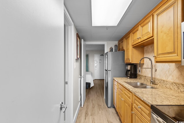 kitchen featuring light stone countertops, light wood-type flooring, tasteful backsplash, stainless steel appliances, and sink