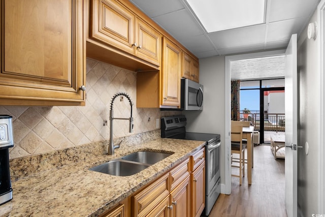 kitchen with a drop ceiling, sink, appliances with stainless steel finishes, light hardwood / wood-style floors, and light stone counters