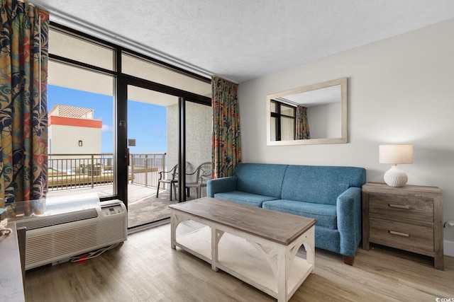 living room with floor to ceiling windows, a wall mounted air conditioner, a textured ceiling, and light wood-type flooring