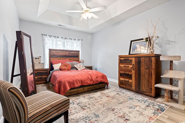 bedroom with a tray ceiling, ceiling fan, and wood-type flooring