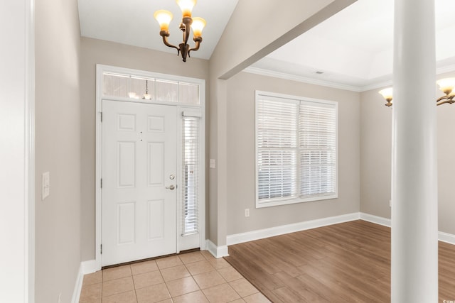 foyer entrance featuring a notable chandelier, light wood-type flooring, crown molding, and decorative columns