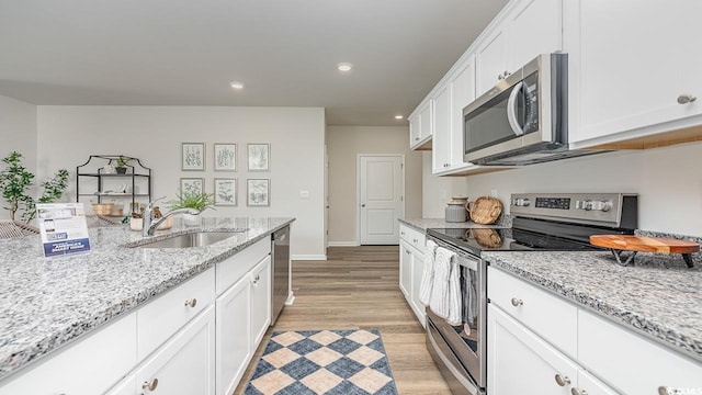 kitchen featuring sink, light hardwood / wood-style flooring, appliances with stainless steel finishes, white cabinetry, and light stone countertops